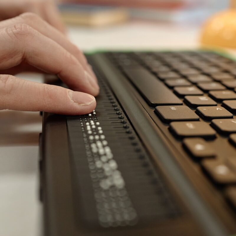 closeup on a hand that is using a keyboard that can type in braille